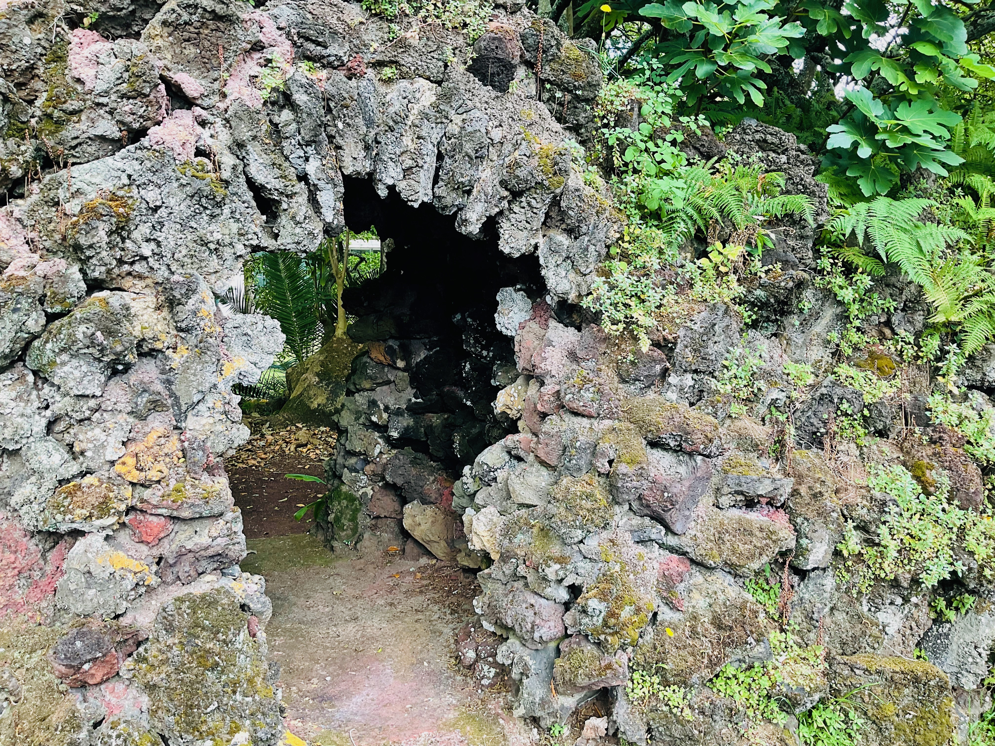 An arch made of volcanic rock spanning a small walkway, with ferns, moss, and other plants sprouting from the rocks.