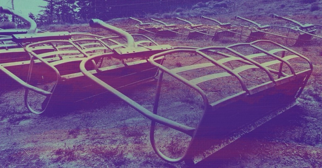 Ski lift benches laid out in tidy rows on the bare earth in summer. Paint strokes over the photo give a suggestion of rust to the otherwise monochromatic scene
